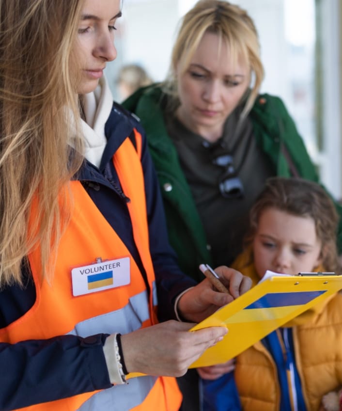 Ein Katastrophenhelfer hält ein Klemmbrett in der Hand, während Mutter und Kind zuschauen.